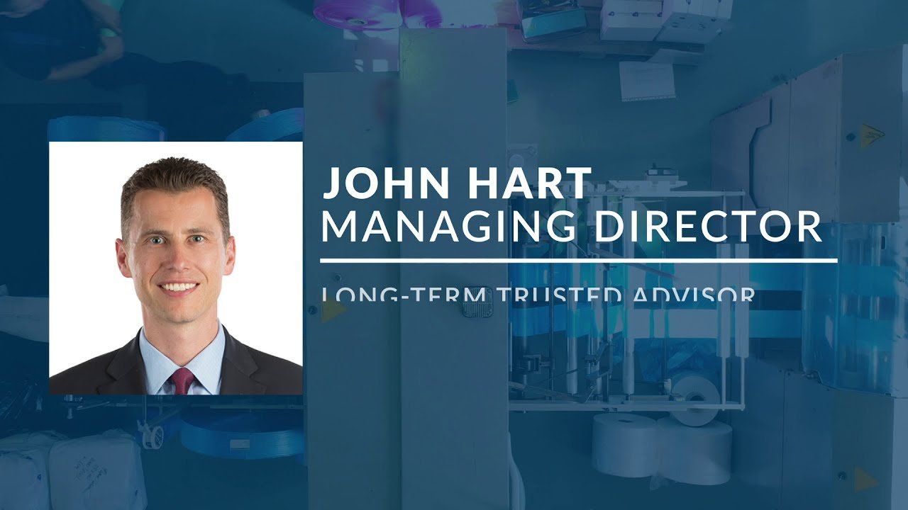 Video still, a managing director headshot card over duotone blue footage of a manufacturing line, with an animated name and title lower third